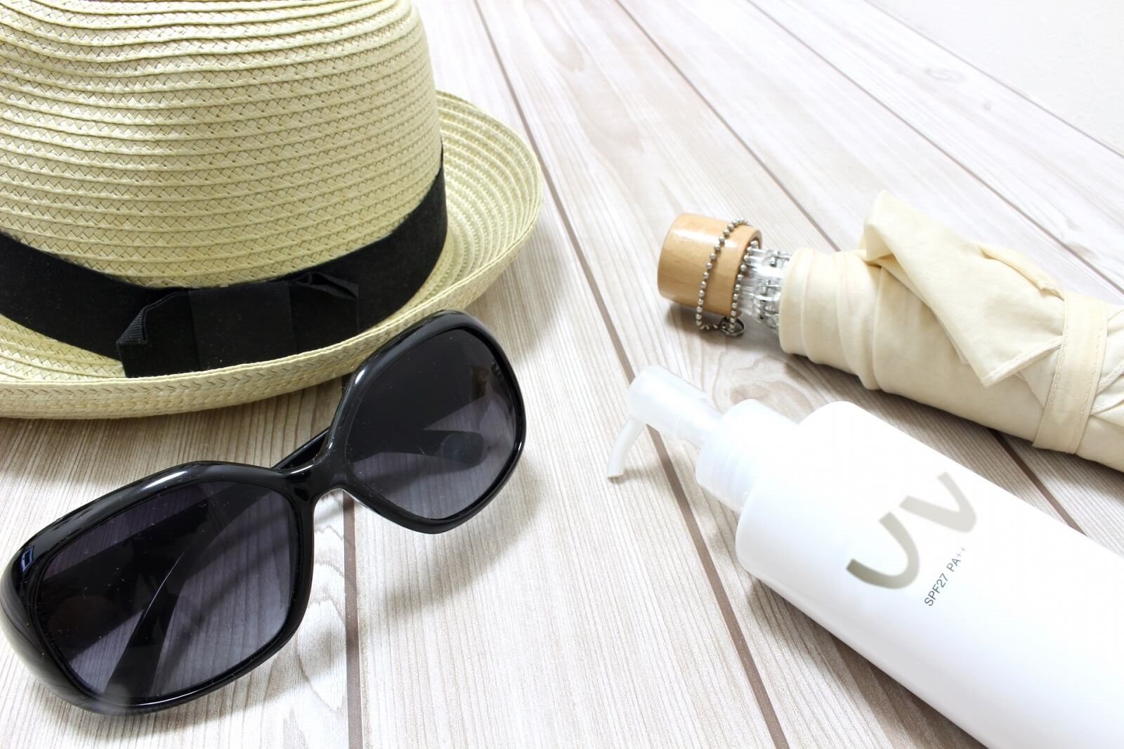 夏にあると便利な持ち物。麦わら帽子、サングラス、日傘、日焼け止めを並べた描写